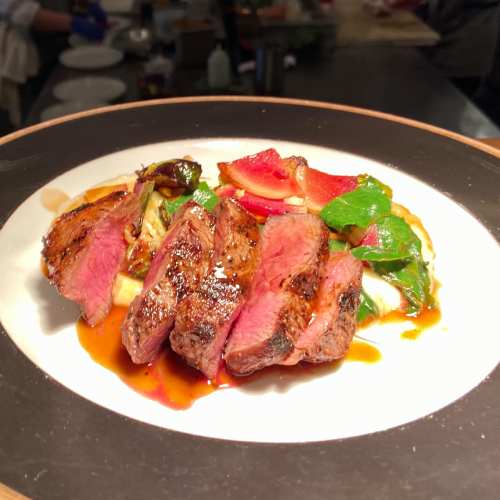 A plate of sliced steak with colorful vegetables and a drizzle of sauce, presented elegantly.