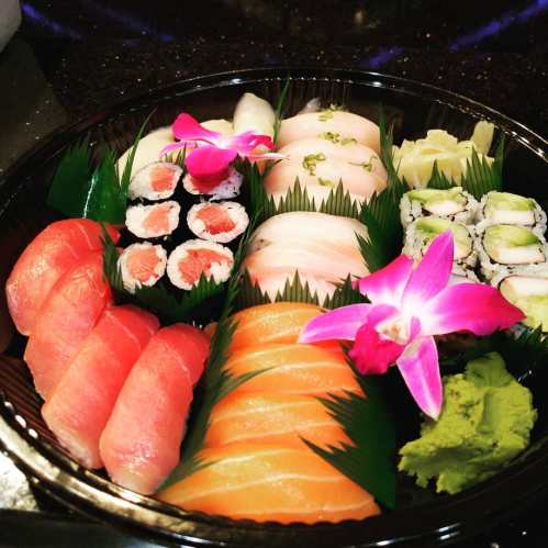 A colorful sushi platter featuring various rolls, sashimi, and garnished with an orchid and wasabi.