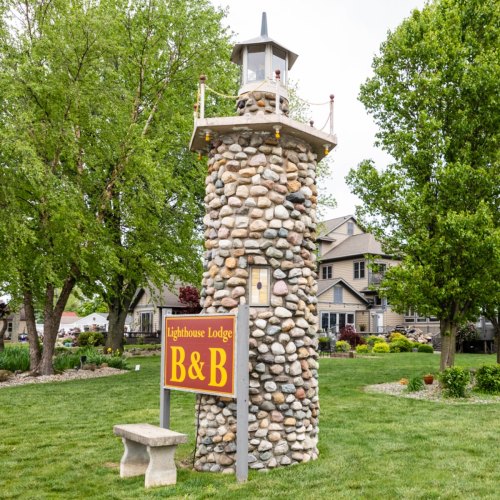 A stone lighthouse structure with a sign reading "Lighthouse Lodge" surrounded by green trees and a grassy area.
