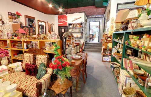 A cozy vintage shop filled with antiques, furniture, and decorative items, featuring a welcoming tea room in the background.