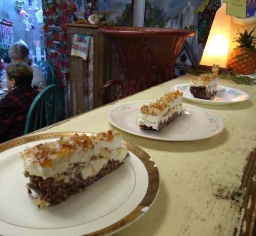 Three slices of layered dessert on plates, with a cozy café background featuring a woman sitting at a table.