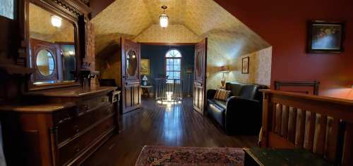 Cozy attic room with wooden furniture, a mirror, and large windows letting in natural light. Warm, inviting atmosphere.