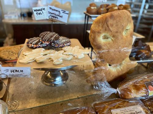 A display of baked goods featuring whoopie pies, mummy cookies, and a large, unique bread shape.