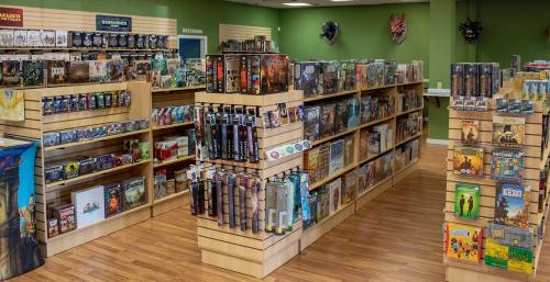 A brightly lit game store with wooden shelves filled with various board games and tabletop games.