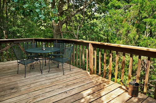 A wooden deck surrounded by trees, featuring a round table and four chairs, creating a serene outdoor space.