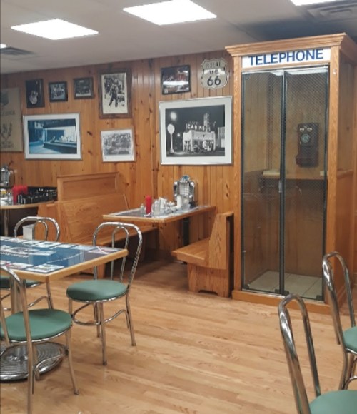A cozy diner interior with wooden walls, vintage decor, tables, and a classic phone booth in the corner.