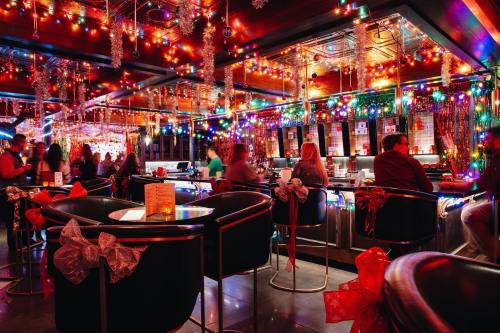 A vibrant bar decorated with colorful lights and festive bows, filled with people enjoying the lively atmosphere.
