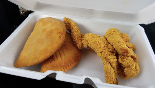 A takeout container with two golden empanadas and several crispy chicken tenders.