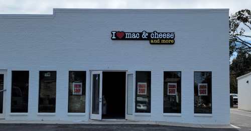 Exterior of a white building with a sign that reads "I ❤️ mac & cheese and more," featuring large windows.