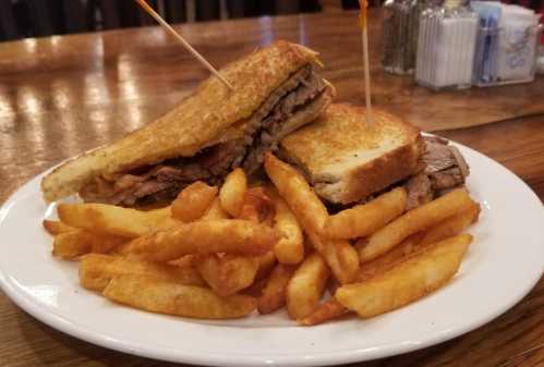 A plate with a grilled sandwich filled with meat and two toothpicks, served with a side of golden French fries.