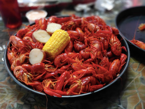 A large platter filled with red crawfish, corn, and sliced potatoes on a table.