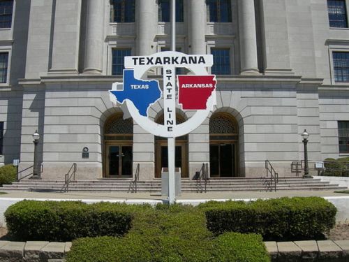 Sign marking the Texas-Arkansas state line in Texarkana, with a building in the background.