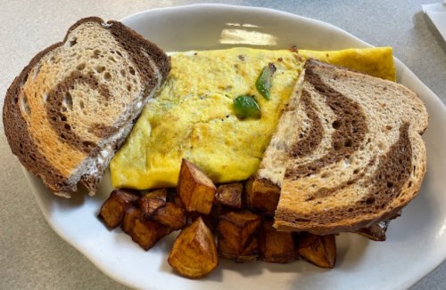 A plate with a fluffy omelet, golden potatoes, and two slices of marbled rye bread.
