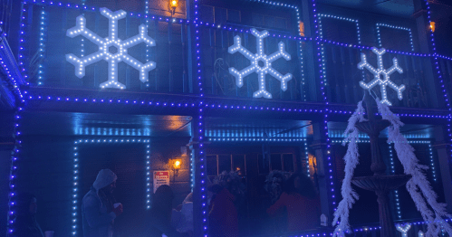 A festive display with blue lights and snowflake decorations on a building, with people gathered below.