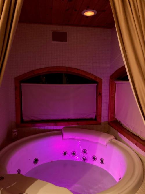 A cozy, dimly lit hot tub with purple lighting, surrounded by curtains and wooden accents.