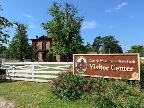 Historic Washington State Park Visitor Center sign in front of a large building and green trees under a clear blue sky.