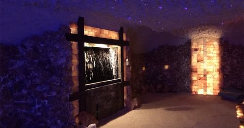 A serene salt room with illuminated salt walls, a water feature, and soft lighting creating a calming atmosphere.