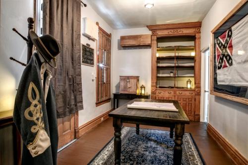 A historical room featuring a coat on a rack, a wooden table, and shelves, with curtains and a flag on the wall.