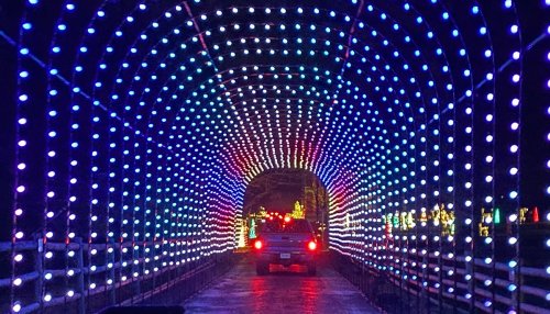 A car drives through a colorful, illuminated tunnel of lights, creating a festive atmosphere.