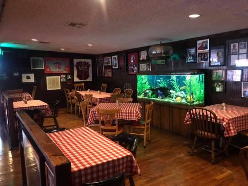 Cozy restaurant interior with checkered tablecloths, wooden chairs, and a large aquarium against a dark wood wall.