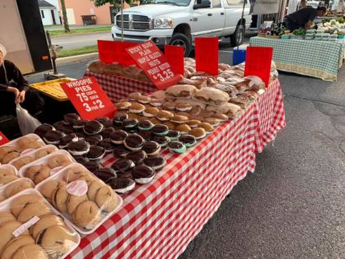 A table at a market displaying various whoopie pies and baked goods, with prices on red signs.