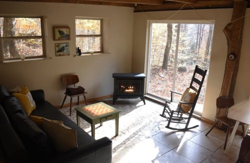 Cozy interior with a black sofa, rocking chair, and a small table, featuring a window view of a forest.