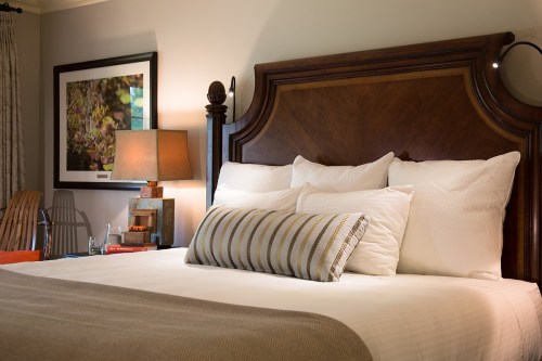 Cozy bedroom featuring a wooden headboard, plush pillows, and warm lighting with decorative artwork on the wall.