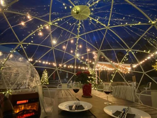 Cozy dining setup inside a geodesic dome, adorned with string lights and festive decorations, with wine glasses on the table.