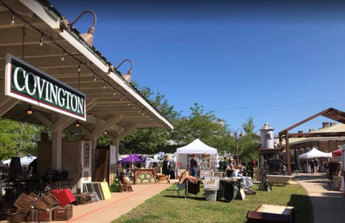 A vibrant outdoor market scene with vendor tents, rustic decor, and a clear blue sky in Covington.