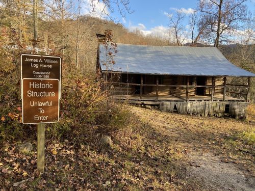 A log house with a metal roof surrounded by trees, featuring a sign that reads "Historic Structure Unlawful To Enter."