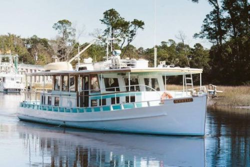 A white boat with teal accents floats on calm water, surrounded by trees and a peaceful landscape.