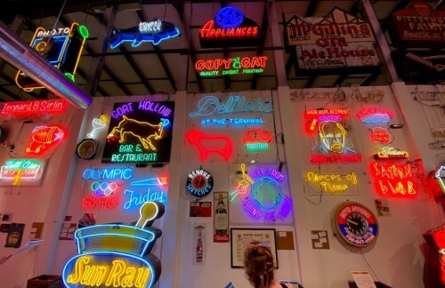 A vibrant display of vintage neon signs on a wall, showcasing various businesses and restaurants in bright colors.
