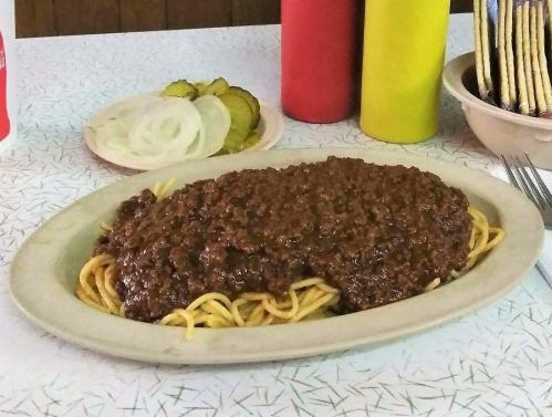 A plate of spaghetti topped with a rich meat sauce, served with pickles and sliced onions on the side.