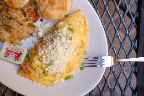 A plate with a cheese omelet topped with green onions, alongside hash browns and a biscuit. A fork rests on the plate.