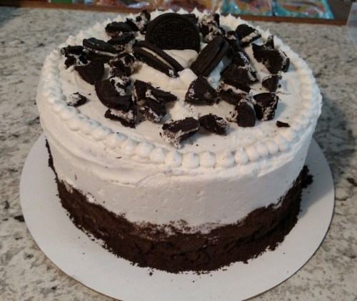 A round cake with white frosting, topped with crushed Oreos and a whole Oreo cookie in the center.