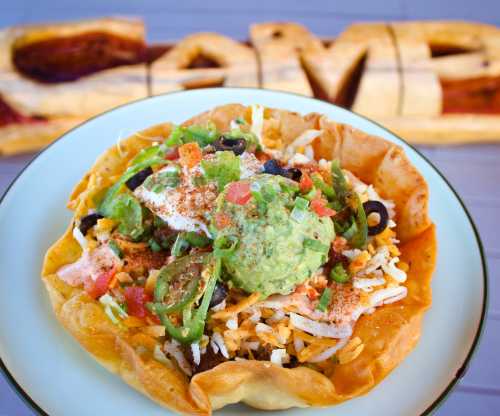 A colorful taco salad in a crispy shell, topped with guacamole, cheese, olives, and fresh vegetables.