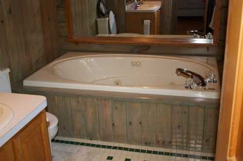 A bathroom featuring a large oval bathtub, wooden paneling, a mirror, and a toilet in the background.