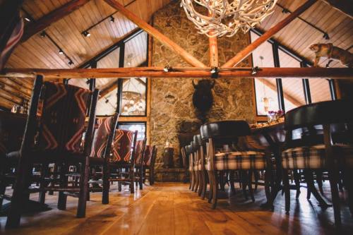 Cozy dining area with wooden beams, stone wall, and rustic chairs, featuring a chandelier and decorative accents.