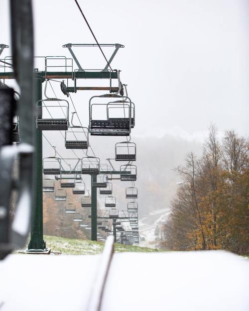 A snow-covered ski lift with empty chairs, surrounded by trees and a misty landscape.
