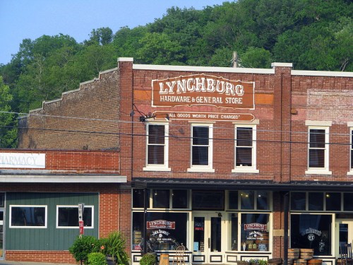 Historic brick storefront of Lynchburg Hardware & General Store, with green accents and a pharmacy sign nearby.