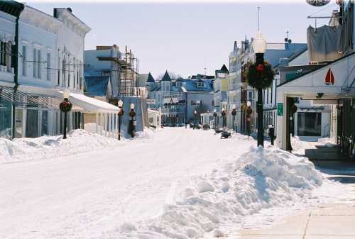 Snow-covered street lined with buildings, decorated with wreaths, under a clear blue sky.