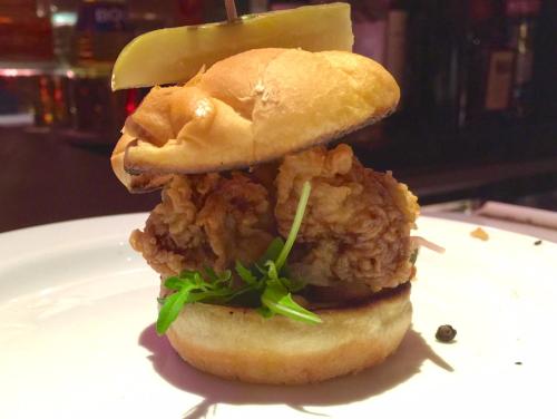 A close-up of a fried chicken sandwich with lettuce and a pickle on top, served on a toasted bun.