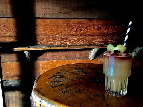 A cocktail with a striped straw sits on a wooden table against a rustic wooden backdrop.