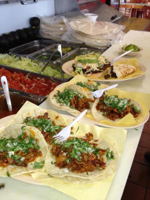 A variety of tacos topped with onions and cilantro, served with tortillas, lettuce, tomatoes, and a side of lime.