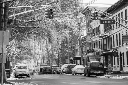 A snowy street scene with traffic lights, parked cars, and storefronts along Union Street in black and white.