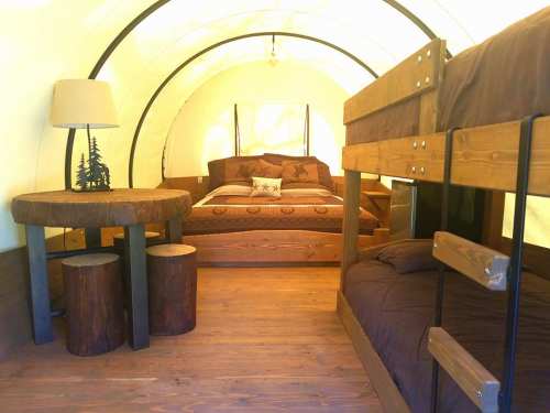 Cozy interior of a glamping tent featuring a double bed, bunk beds, and rustic wooden furniture.