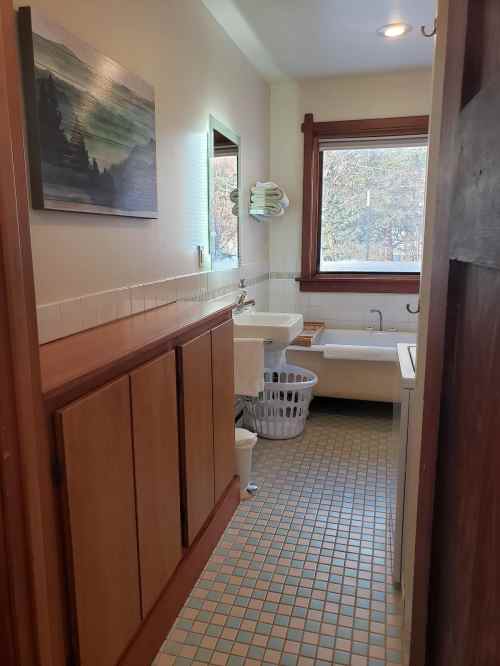 A bright bathroom with a sink, toilet, and bathtub, featuring wooden accents and a window with natural light.