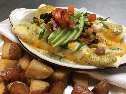 A plate of enchiladas topped with avocado, pico de gallo, and cheese, served with crispy potato wedges.