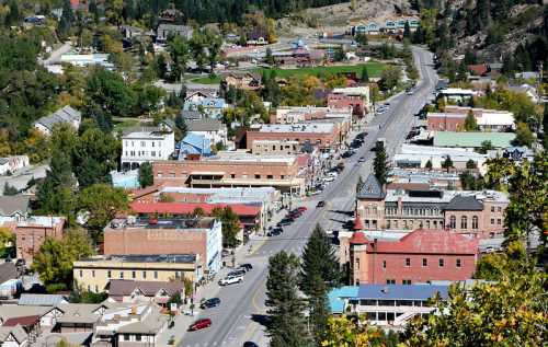 Aerial view of a small town with colorful buildings, trees, and a main road lined with cars.