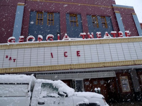 Snow falls on the Georgia Theatre, with a marquee displaying "ICE" and a snow-covered vehicle in the foreground.